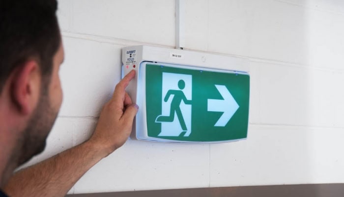 Professional checking the functionality of an emergency exit light during a routine inspection and maintenance service in Melbourne