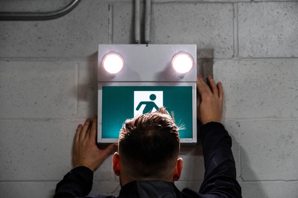 Technician performing a maintenance check on an emergency exit light system using advanced technology to ensure quality and reliability at a Melbourne property